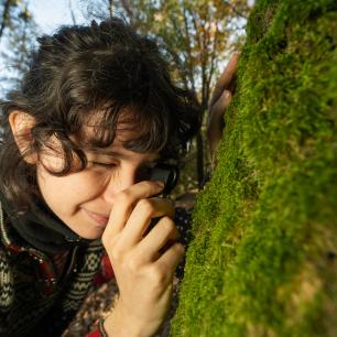 Woman examining moss on a tree trunk with a magnifying glass.