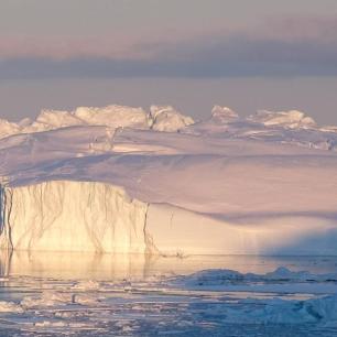 Icebergs floating in water, under a cloudy sky.