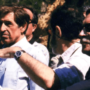 Men in a group, one pointing with his hand.