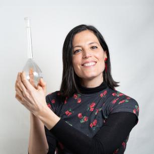 Woman smiling, holding a transparent glass item against a white backdrop.
