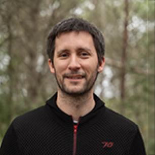 Smiling man in black sweater, forest background.