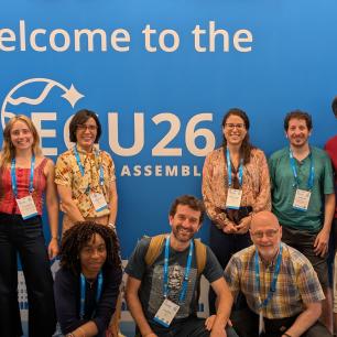 Group of people posing in front of a blue backdrop, smiling.