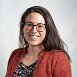 Woman with glasses smiling, wearing a rust-colored cardigan.