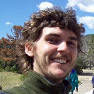 Smiling man with curly brown hair against a blue sky.