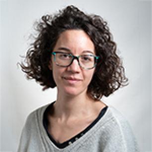 Woman with curly hair and glasses, looking at the camera.