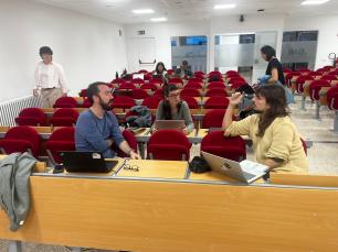 People in a lecture hall with red chairs and open laptops.