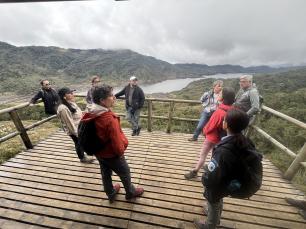 Group of people on a wooden platform overlooking a lake and mountains.