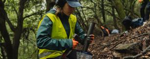 Woman in safety vest and hat hammering tool.