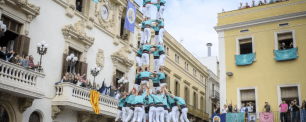 People building a human tower in front of buildings.