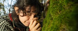 Woman examining moss on a tree trunk with a magnifying glass.