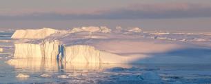 Icebergs floating in water, under a cloudy sky.