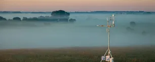 Weather station in a field with morning fog.