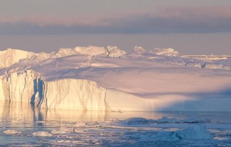 Icebergs floating in water, under a cloudy sky.