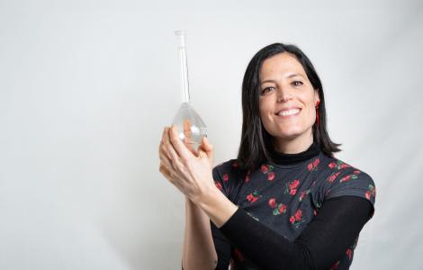 Woman smiling, holding a transparent glass item against a white backdrop.
