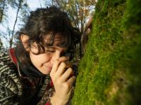 Woman examining moss on a tree trunk with a magnifying glass.