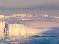 Icebergs floating in water, under a cloudy sky.