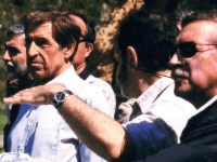 Men in a group, one pointing with his hand.