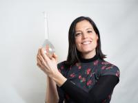 Woman smiling, holding a transparent glass item against a white backdrop.