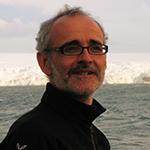 Man wearing glasses with a glacier in the background.