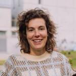 Woman with curly hair smiling brightly; blurred background.