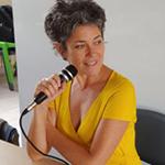 Woman with microphone, yellow dress, and short gray hair.