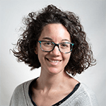 Woman with curly hair and glasses smiling at the camera.