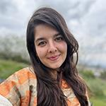 Smiling woman with long brown hair, wearing orange patterned shirt.