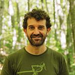 Man smiling at camera in front of a forest.