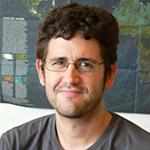 Man with glasses smiles, map in background.