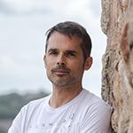 Man leaning against a stone wall, looking thoughtful.