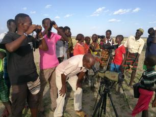 Group of people birdwatching, using binoculars and scopes.