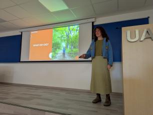 Woman presenting in a classroom, pointing at a projection screen.