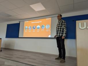 Man in checked shirt standing next to a presentation screen in a classroom.