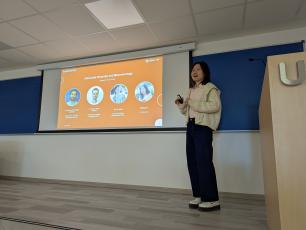 Woman presenting in front of a screen displaying graphics.