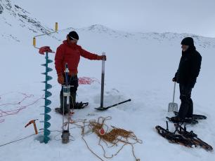 Two men collecting ice samples in snowy terrain. 