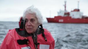 Woman in life jacket on boat with a red ship in the background.