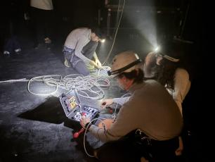 Persones amb frontals que treballen amb cordes i equipament de campament a l'escenari.