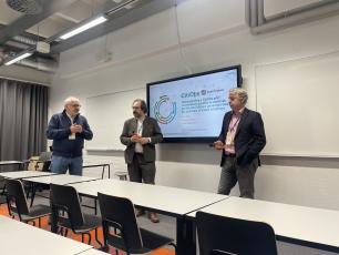 Three men standing in front of a screen in a classroom setting.