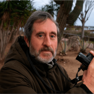 Middle-aged man holding camera outdoors.