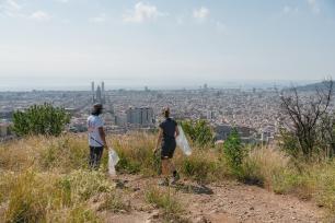 Two people picking up trash on a hill overlooking a city.